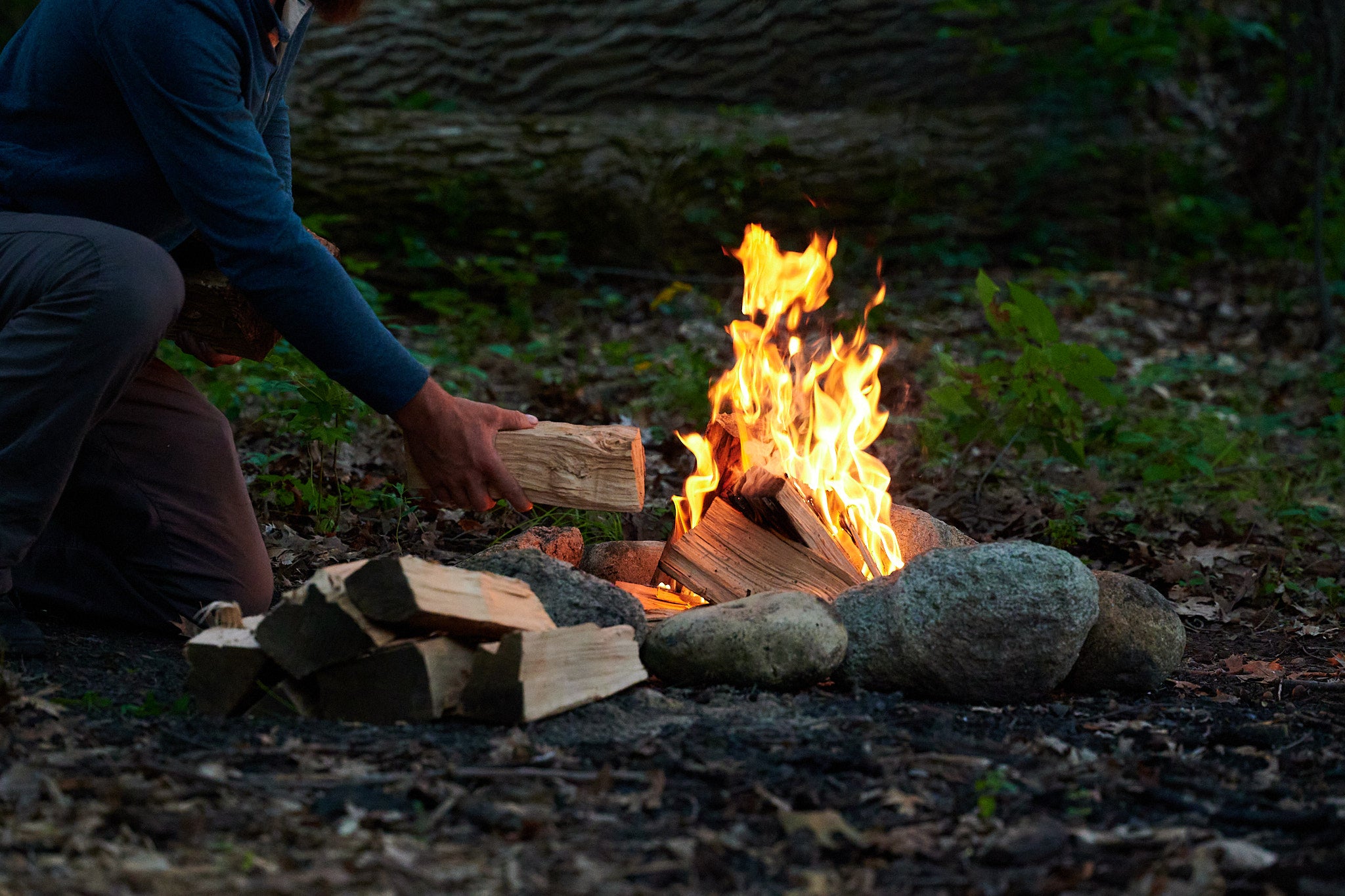 Adding wood to a campfire outdoors